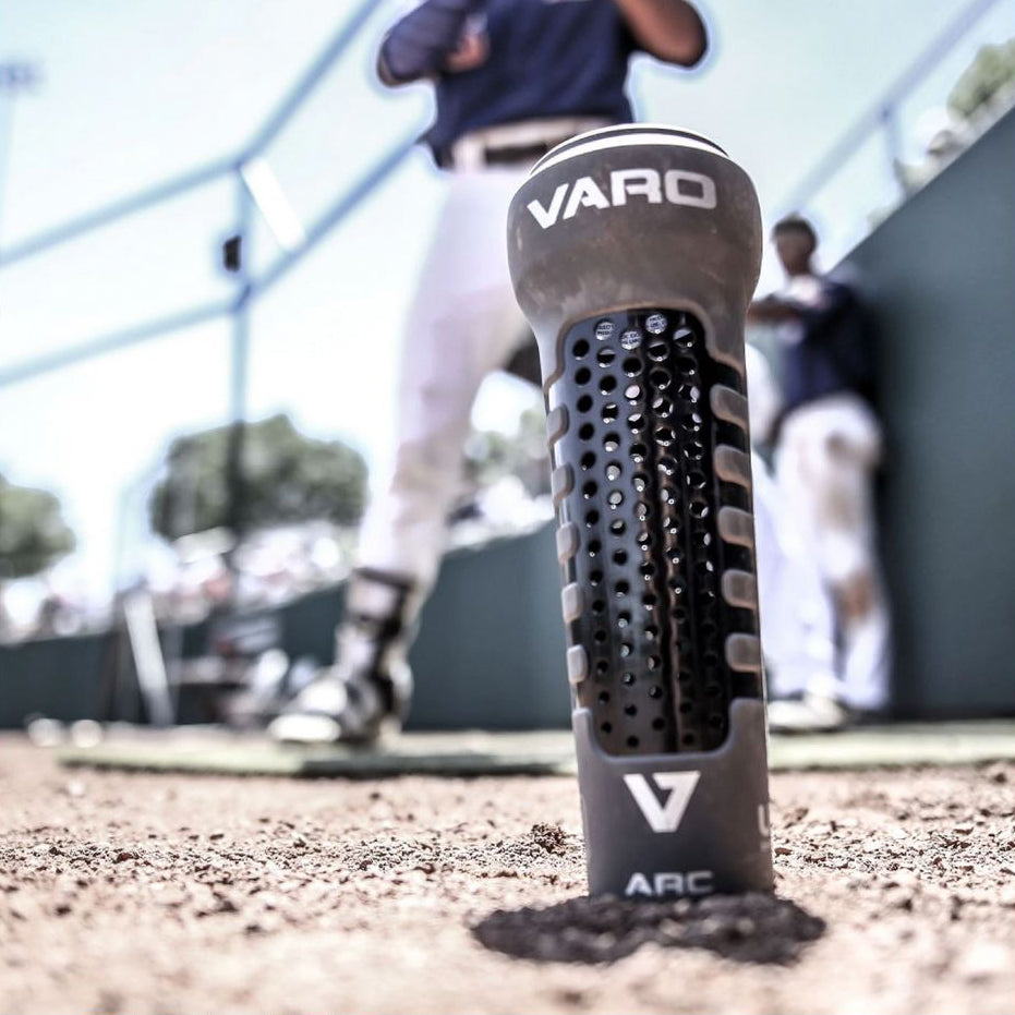 A baseball player stands in the dirt, focusing on swing mechanics and using the Varo ARC 12 oz Bat Weight (ARCBG/ARCLGSB) to take batting skills to the next level.