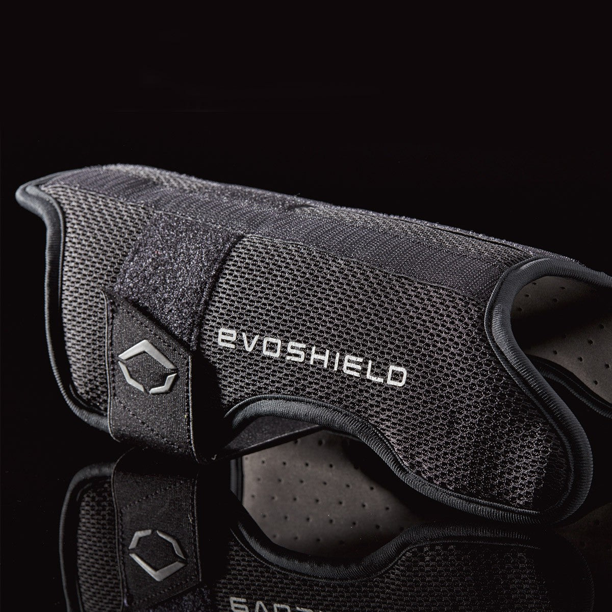 A black EvoShield Pro-SRZ Gel-to-Shell™ Catcher's Lower Leg Guard (WB570800 / WB571030) with textured mesh and Velcro strap is shown on a dark reflective surface. The EvoShield logo is visible, highlighting superior leg protection for catchers.
