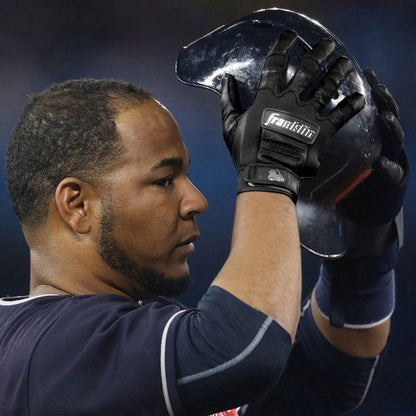 A baseball player in a navy jersey and black Franklin CFX Pro Full Color Chrome Adult Batting Gloves: 205 holds up a black helmet with both hands, partially covering his face.