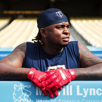 A baseball player in a navy sleeveless shirt, headband, and Franklin CFX Pro Full Color Chrome Adult Batting Gloves: 205 leans on the dugout rail with a Merrill Lynch logo, looking to the side.