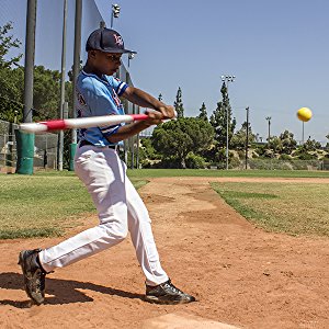 A young player in blue shows off his swing, hitting a PowerNet 3.2" Weighted Hitting and Batting Training Ball (6 Pack): 1004L by PowerNet on a sunny outdoor field.