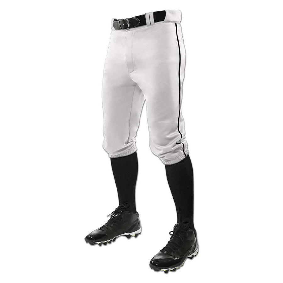 A person wearing Champro Sports Youth Triple Crown Knicker Baseball Pants with Piping (BP101Y), featuring black piping, and paired with a black belt, black knee-high socks, and black cleats stands against a white background.