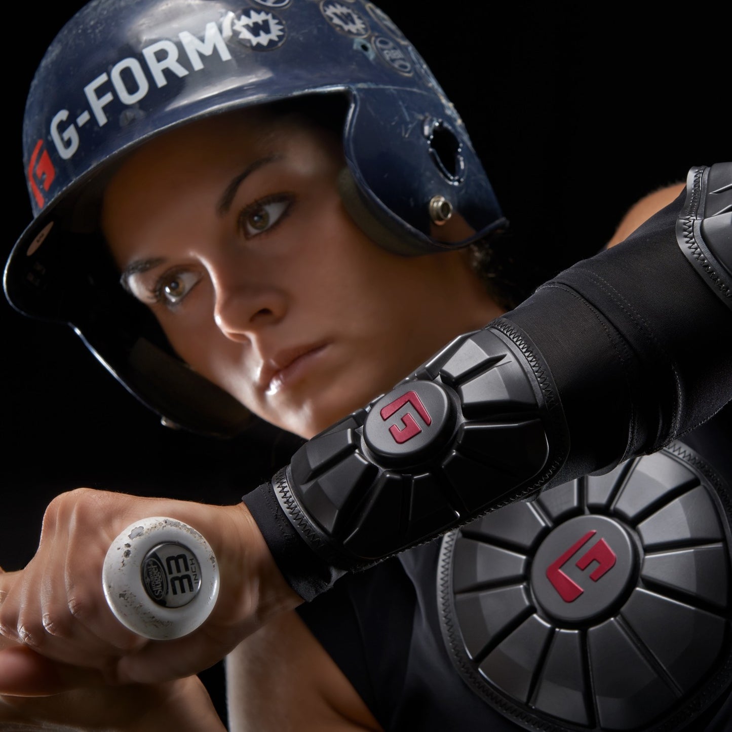 A focused athlete wearing a blue helmet and black gear with red G-Form logos grips a bat, highlighting the advanced impact protection of the G-Form Pro Wrist Guard (WG0102) with visible SmartFlex padding on the arm and chest.