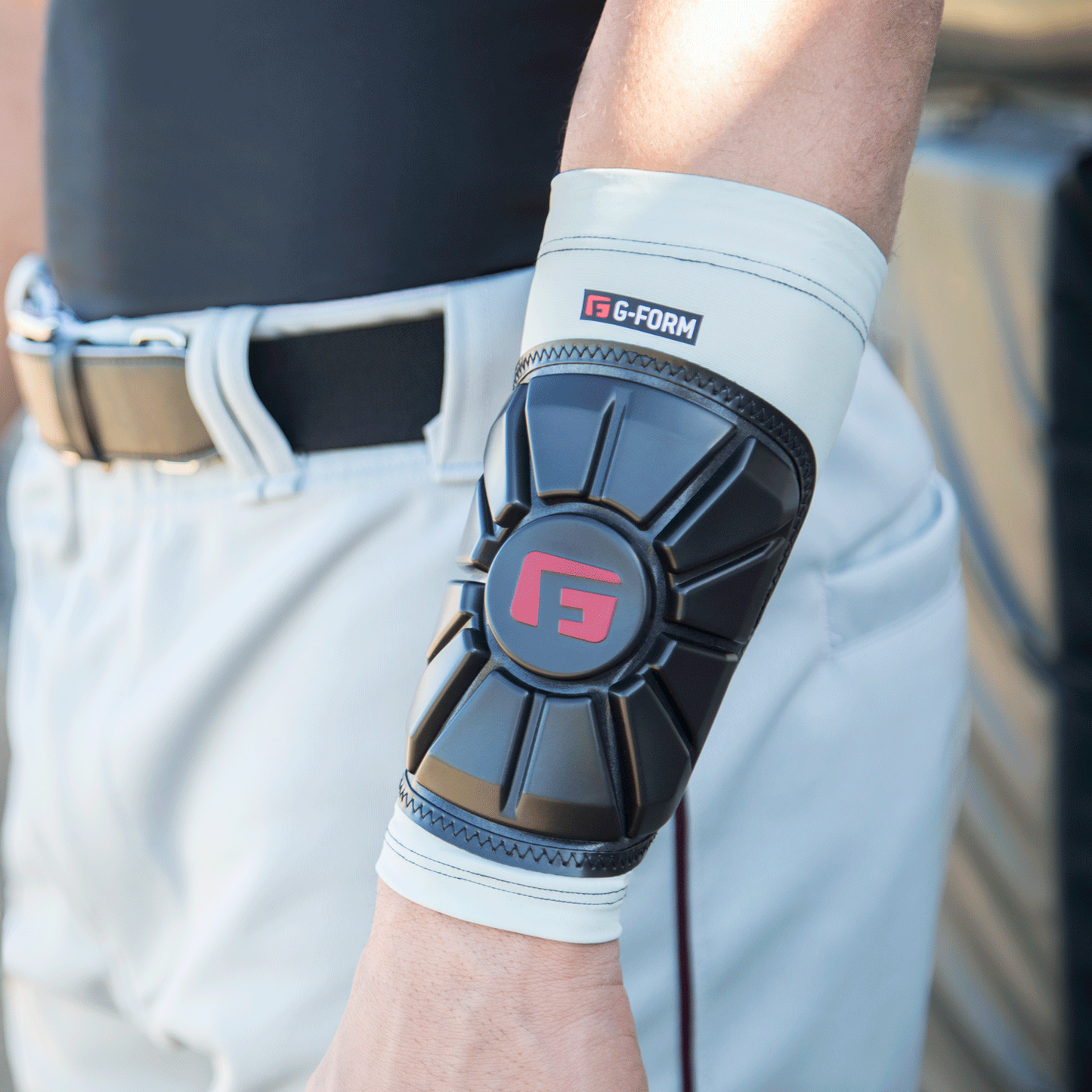 A person in white baseball pants and a black belt is wearing a black G-Form Pro Wrist Guard (WG0102) with SmartFlex pads and visible red and white G-Form branding on their arm.