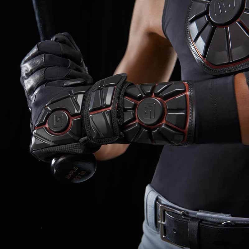 A baseball player in G-Form Pro Wrist Guard (WG0102) grips a bat, wearing black gear and gloves with a gray belt against a dark background for maximum impact protection.